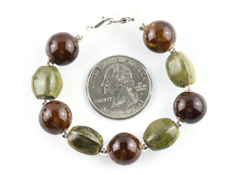 May include: A brown and green ceramic bead bracelet with a silver clasp. The bracelet is about the size of a quarter.