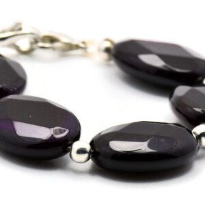 May include: A bracelet made of dark purple agate beads with silver accents. The beads are oval shaped and have a faceted finish.