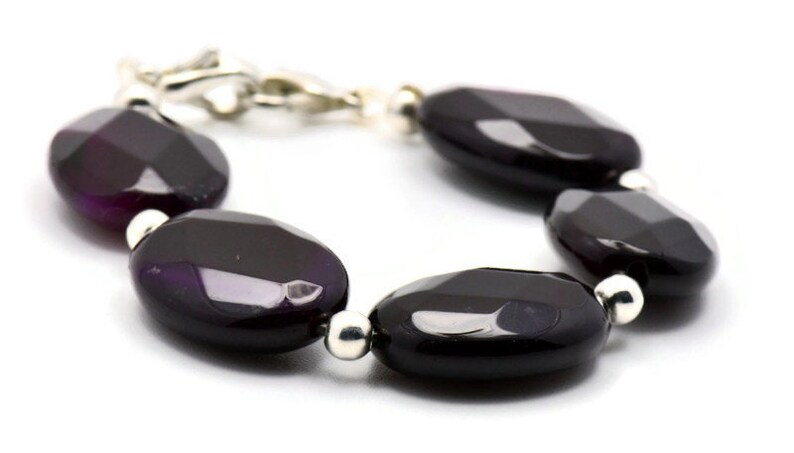 May include: A bracelet made of dark purple agate beads with silver accents. The beads are oval shaped and have a faceted finish.