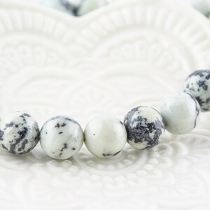 May include: A white and black speckled bracelet made of round beads.