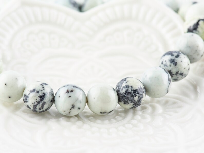 May include: A white and black speckled bracelet made of round beads.
