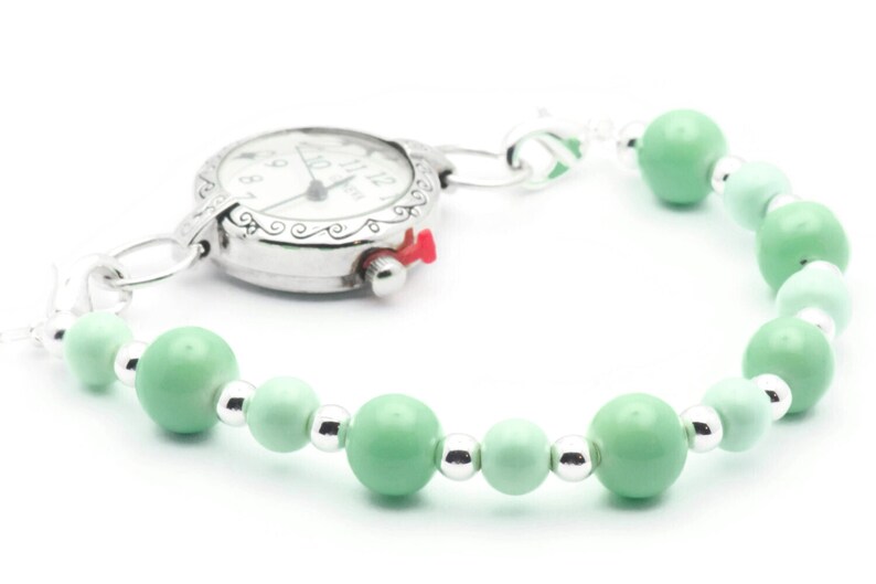 May include: A silver pocket watch with a white face and black hands attached to a green beaded bracelet.