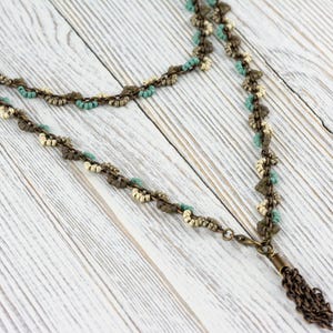 May include: A double-strand necklace with a tassel pendant. The necklace is made of small, white, brown, and turquoise beads. The tassel is made of a chain with a brown finish.