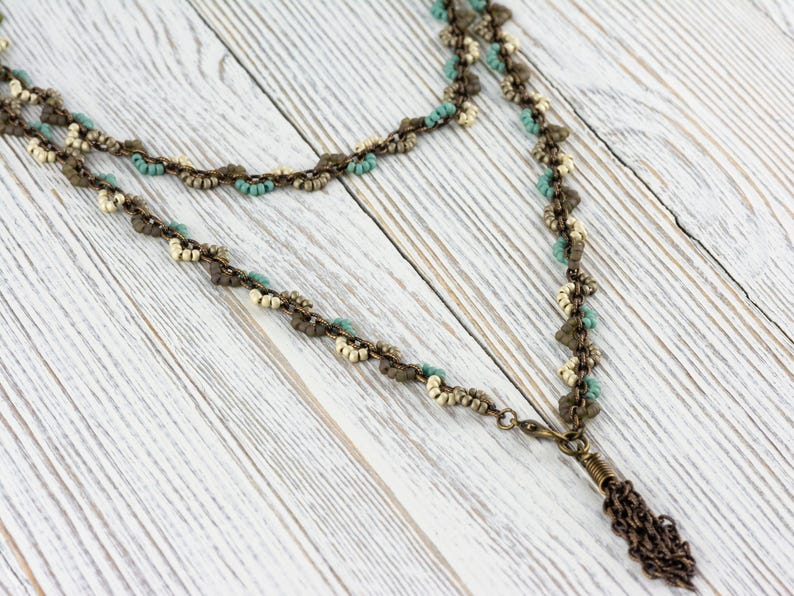 May include: A double-strand necklace with a tassel pendant. The necklace is made of small, white, brown, and turquoise beads. The tassel is made of a chain with a brown finish.