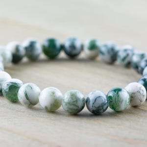 May include: A green and white agate beaded bracelet. The beads are round and have a natural, marbled pattern.