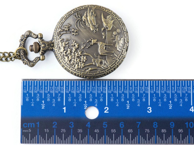 Pu&ograve; includere: Un orologio da tasca in bronzo con un design dettagliato di un cervo, alberi e montagne. L'orologio ha un diametro di 4,5 cm ed &egrave; dotato di una catena.