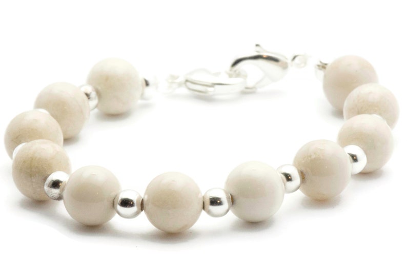 Op de afbeelding: Een witte kralen armband met zilveren accenten. De armband is gemaakt van ronde, gladde kralen en heeft een zilveren sluiting.
