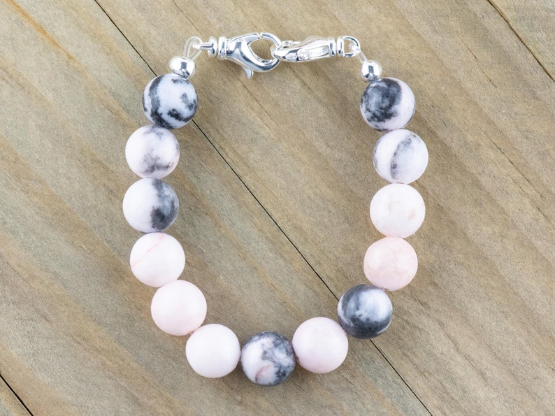 May include: A pink and black gemstone bracelet with a silver clasp. The bracelet is made of round beads and is approximately 18 cm long.