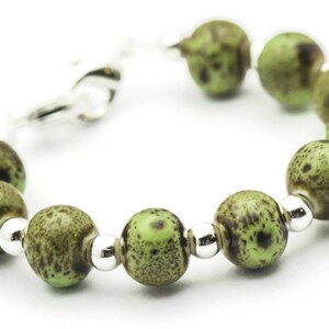 May include: A green and brown speckled bead bracelet with silver accents. The bracelet is made of round beads and has a clasp closure.