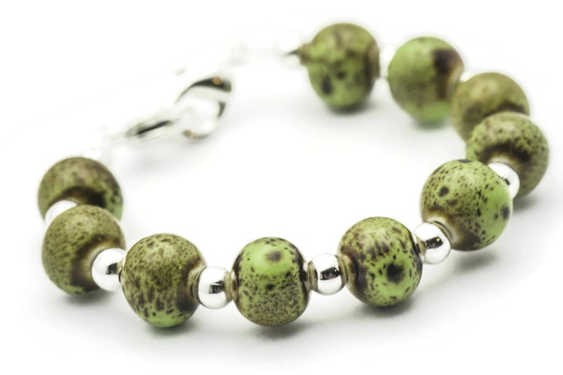 May include: A green and brown speckled bead bracelet with silver accents. The bracelet is made of round beads and has a clasp closure.
