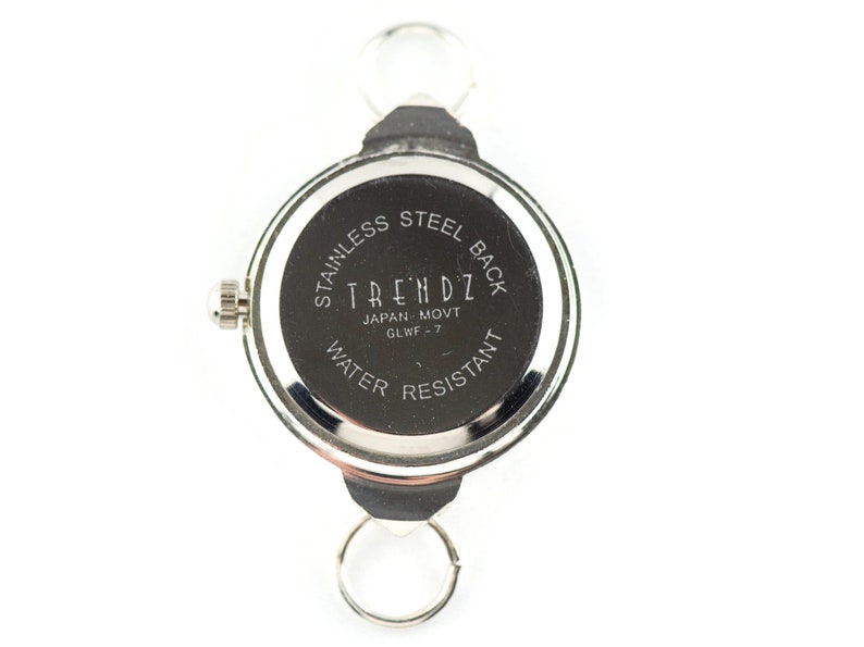 Peut inclure: Dos d'une montre argent&eacute;e avec un cadran noir. Le cadran de la montre indique "Stainless Steel Back", "Trendz", "Japan Movt", "GLWF - 7", et "Water Resistant".