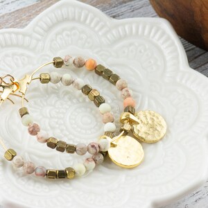 May include: Gold hoop earrings with a hammered gold charm and a mix of white, pink, and brown beads.