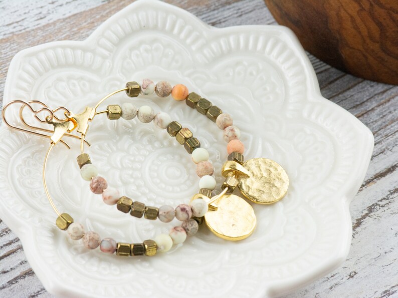 May include: Gold hoop earrings with a hammered gold charm and a mix of white, pink, and brown beads.