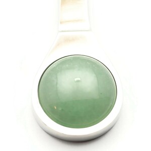 Puede incluir: Un colgante de plata con una piedra preciosa redonda de color verde claro.