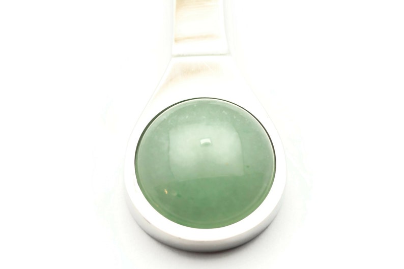Puede incluir: Un colgante de plata con una piedra preciosa redonda de color verde claro.