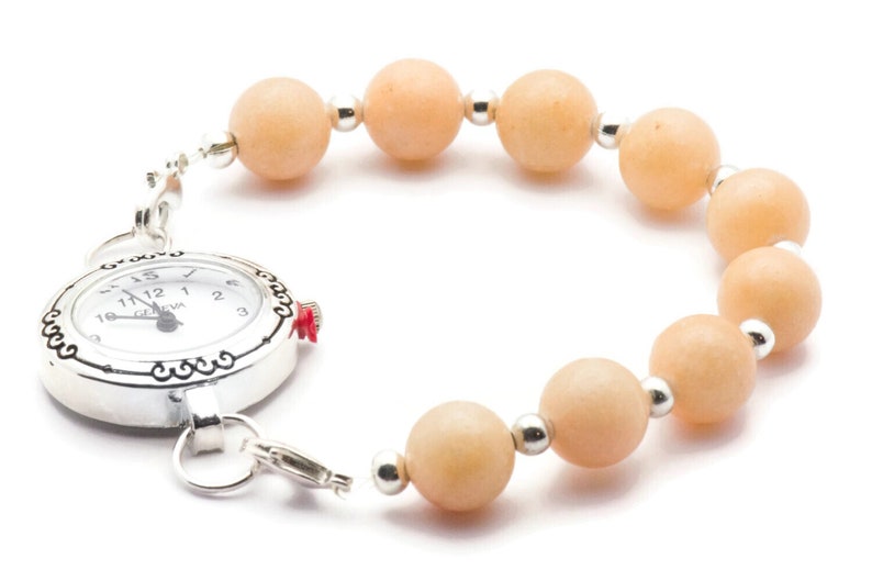 Puede incluir: Un reloj plateado con una esfera blanca y n&uacute;meros negros est&aacute; unido a una pulsera hecha de cuentas de color naranja claro.