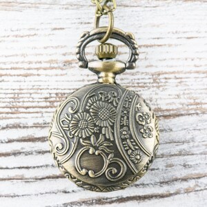 May include: A gold-toned pocket watch with an ornate floral design. The watch has a chain attached to the top.