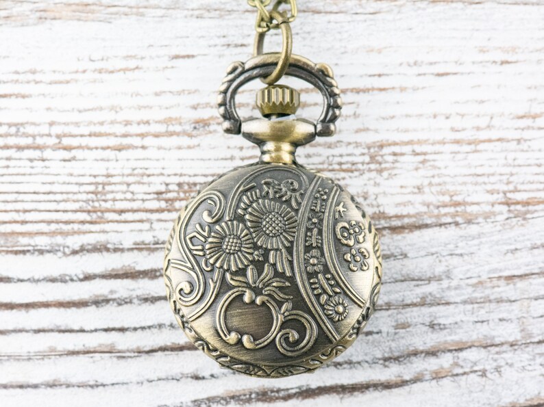 May include: A gold-toned pocket watch with an ornate floral design. The watch has a chain attached to the top.