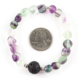 Puede incluir: Un brazalete hecho con cuentas de fluorita verde, p&uacute;rpura y blanca y una cuenta de lava negra. El brazalete es aproximadamente del tama&ntilde;o de una moneda de 25 centavos de d&oacute;lar estadounidense.