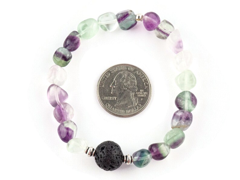 Puede incluir: Un brazalete hecho con cuentas de fluorita verde, p&uacute;rpura y blanca y una cuenta de lava negra. El brazalete es aproximadamente del tama&ntilde;o de una moneda de 25 centavos de d&oacute;lar estadounidense.