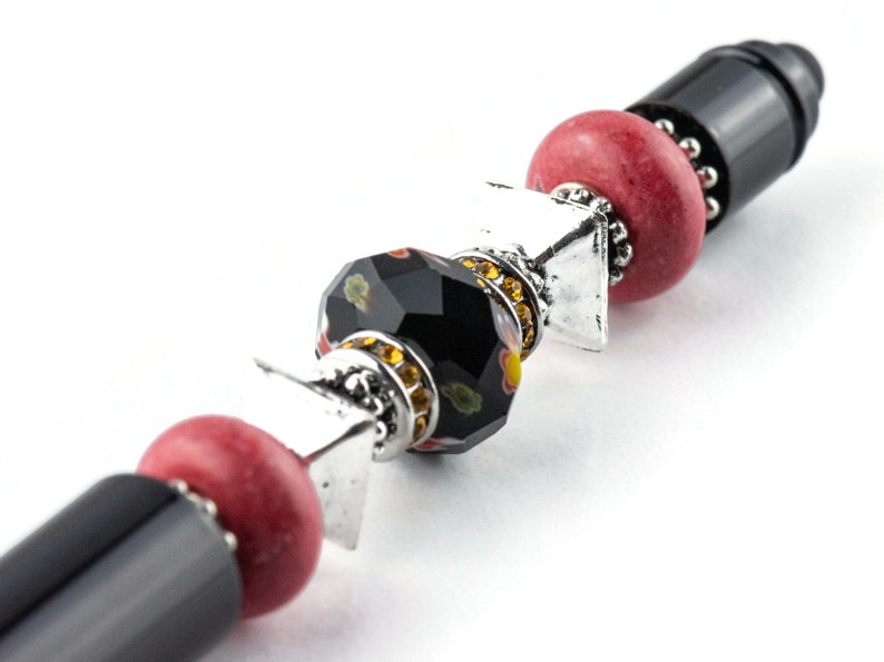 May include: A black and red beaded pen with silver accents. The pen has a black barrel with a red bead, a black bead with gold and red accents, a silver spacer, and a red bead.