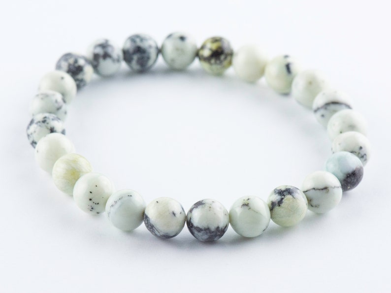 May include: A white and black speckled stone bracelet with a round shape. The bracelet is made of natural stones and is a popular choice for jewelry.