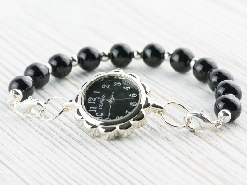 May include: A black beaded bracelet with a silver watch face that says "GENEVA" and has black hands and numbers.