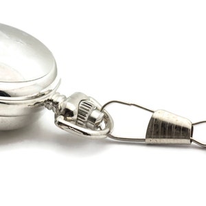 May include: A silver pocket watch with a chain attached. The watch has a round face and a hinged lid.