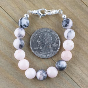 May include: A pink and grey gemstone bracelet with a silver clasp. The bracelet is about the size of a 25 pence coin.
