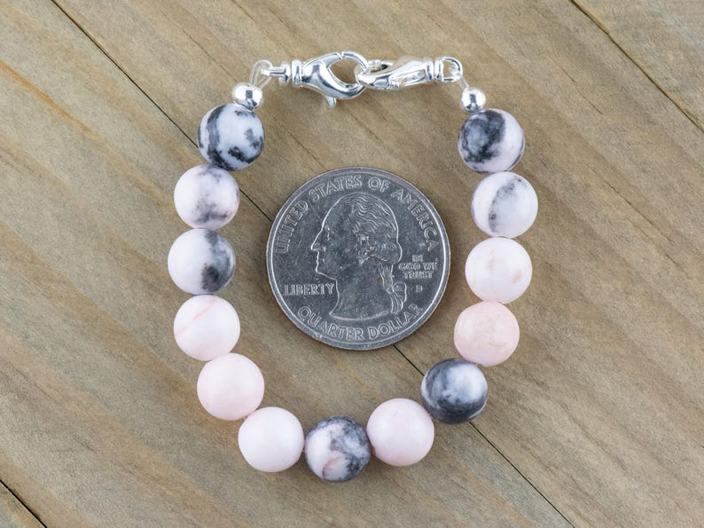 May include: A pink and grey gemstone bracelet with a silver clasp. The bracelet is about the size of a 25 pence coin.