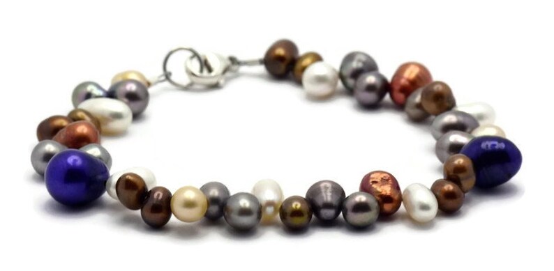 May include: A multi-colored freshwater pearl bracelet with a silver clasp. The pearls are in shades of white, cream, gray, brown, copper, and blue.