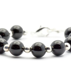 Puede incluir: Una pulsera con grandes cuentas negras brillantes intercaladas con cuentas plateadas m&aacute;s peque&ntilde;as. La pulsera est&aacute; unida con un cierre plateado, creando un dise&ntilde;o simple pero elegante. Las cuentas tienen aproximadamente 1,3 cm de di&aacute;metro.