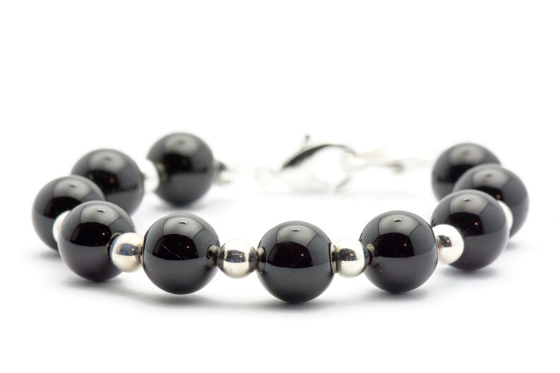 Puede incluir: Una pulsera con grandes cuentas negras brillantes intercaladas con cuentas plateadas m&aacute;s peque&ntilde;as. La pulsera est&aacute; unida con un cierre plateado, creando un dise&ntilde;o simple pero elegante. Las cuentas tienen aproximadamente 1,3 cm de di&aacute;metro.