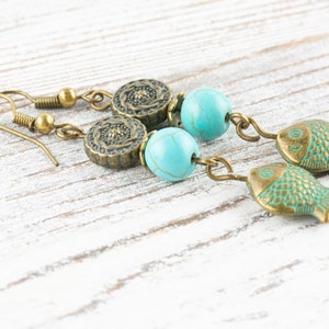 May include: A pair of dangle earrings with turquoise beads and bronze fish charms. The earrings have a floral design on the top of the beads.