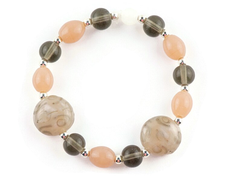 May include: A bracelet featuring alternating light pink and dark grey beads. The bracelet includes two larger, round, grey beads with a swirling pattern.