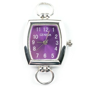 May include: A silver watch with a purple face and white numbers. The watch has a rectangular shape and a Geneva logo on the face.