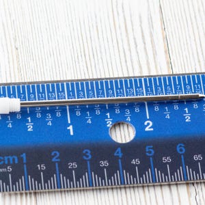 Puede incluir: Una regla de metal plateado con marcas azules y n&uacute;meros negros. La regla est&aacute; marcada en pulgadas y cent&iacute;metros. Un bol&iacute;grafo de metal plateado est&aacute; sobre la regla.