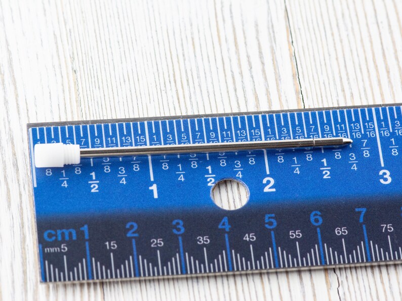 Puede incluir: Una regla de metal plateado con marcas azules y n&uacute;meros negros. La regla est&aacute; marcada en pulgadas y cent&iacute;metros. Un bol&iacute;grafo de metal plateado est&aacute; sobre la regla.
