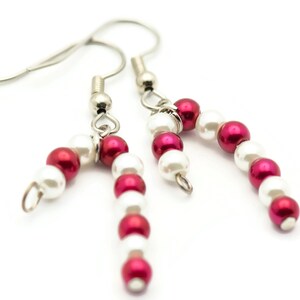 May include: A pair of silver dangle earrings with red and white beads, resembling candy canes.