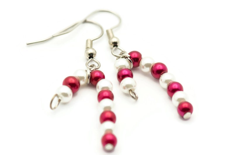 May include: A pair of silver dangle earrings with red and white beads, resembling candy canes.