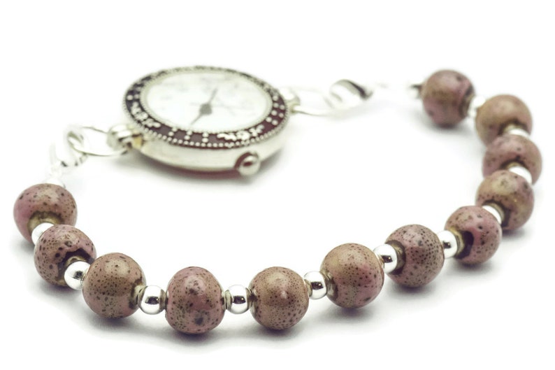 May include: A silver watch with a white face and black markings is attached to a bracelet made of brown beads with silver accents.
