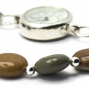 May include: A silver watch with a white face and a brown and green stone bracelet.