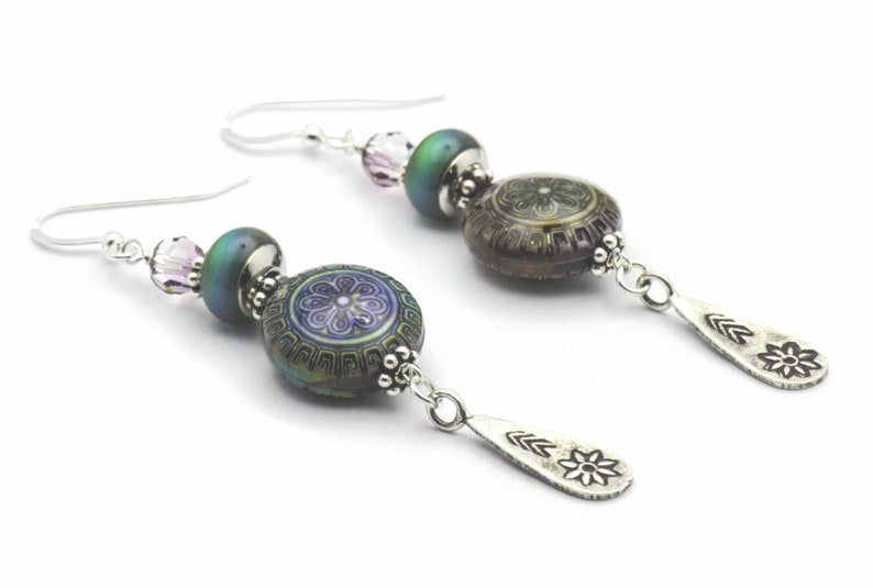 May include: Silver dangle earrings featuring a purple and green iridescent glass bead, a smaller pink crystal bead, and a silver charm with a flower design.