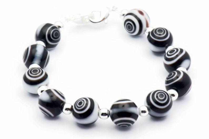 K&ouml;nnte beinhalten: Ein schwarz-wei&szlig;es Armband mit silbernen Perlen und einem Verschluss. Die Perlen haben ein wirbelndes Muster.