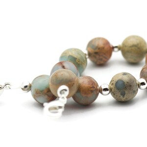 May include: A silver clasp bracelet with brown, green, and white patterned beads.
