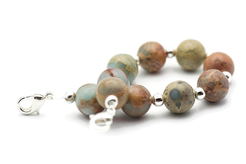 May include: A silver clasp bracelet with brown, green, and white patterned beads.