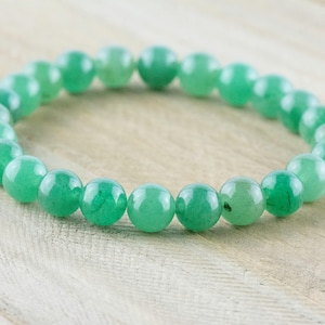 May include: A green gemstone bracelet made of round beads. The bracelet is on a light wood surface.