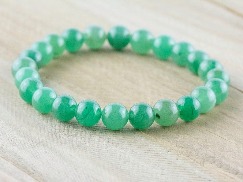 May include: A green gemstone bracelet made of round beads. The bracelet is on a light wood surface.