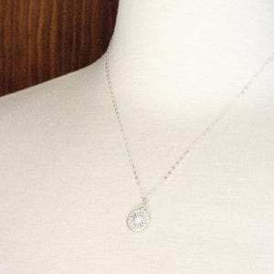 K&ouml;nnte beinhalten: Eine silberne Halskette mit einem zarten, runden Anh&auml;nger mit einem detaillierten, durchbrochenen Design.