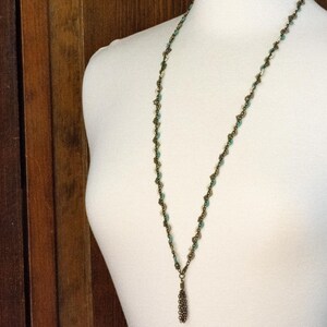 May include: A long, delicate necklace with a bronze chain and turquoise beads. The necklace has a tassel pendant at the bottom.